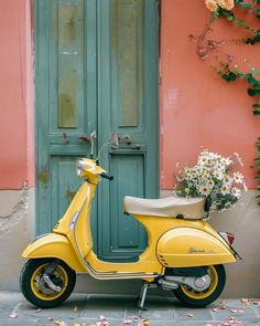 a yellow scooter is parked in front of a pink building with green doors