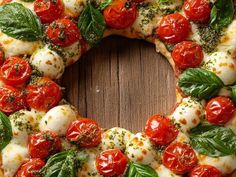 a pizza with tomatoes, mozzarella and spinach leaves on it sitting on a wooden surface