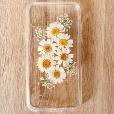 a clear phone case with white and yellow flowers on the front, sitting on a wooden surface