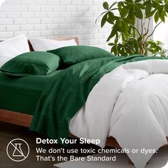 a bed with green sheets and pillows next to a potted plant