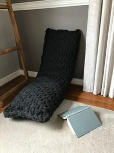 a black crocheted blanket sitting on the floor next to a book and ladder