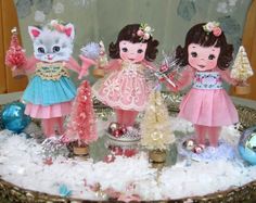 three little dolls are standing in front of a christmas tree with a cat on top