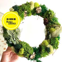 a person holding up a wreath made out of moss and pine cones with the words as seen on better homes above it