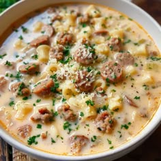 a white bowl filled with pasta and meat soup on top of a wooden table next to broccoli