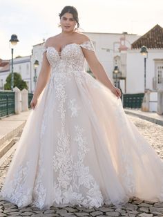 a woman in a wedding dress standing on a cobblestone road with her arms behind her back