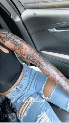 a woman sitting in the back seat of a car with tattoos on her arm and leg