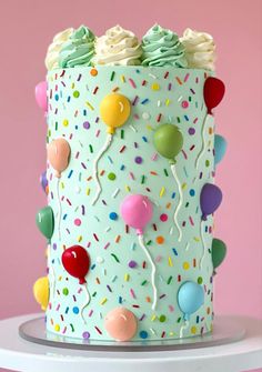 a birthday cake with sprinkles and balloons on the top is decorated in pastel green frosting