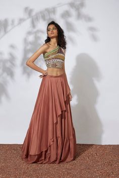 Indulge in the captivating allure of this burnt orange lehenga, featuring a gathered skirt with an asymmetrical drape. The one shoulder crop top is exquisitely embroidered with intricate threads, tubes, pearls, beads, and mirrors, adding a touch of opulence to your ensemble. Prepare to make a statement in this luxurious outfit, reminiscent of the worlds of art, literature, and fashion. Colour : RUST Fabric : CREPE Embroidery details : HAND EMBROIDERY Components : 2 Wash Care : DRY CLEAN ONLY Del Traditional One-shoulder Pre-draped Saree For Reception, Fitted One-shoulder Pre-draped Saree For Designer Wear, One-shoulder Lehenga For Festive Reception, One-shoulder Festive Lehenga For Reception, Festive One-shoulder Lehenga For Reception, Elegant One Shoulder Choli For Festive Season, Elegant One Shoulder Choli For Festive Occasions, Traditional One-shoulder Pre-draped Saree For Designer Wear, Elegant One-shoulder Choli For Festive Occasions