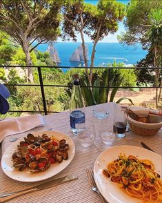 two plates of pasta and clams on an outdoor table overlooking the ocean in capri, italy