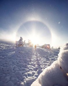 the sun shines brightly over snow covered ground with trees in the distance and people walking through it