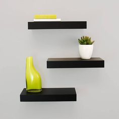 two black floating shelves with green vases and books on them, one is empty