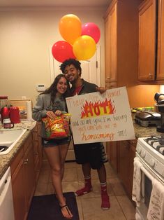 two people standing in a kitchen holding up a sign that says hot and some balloons