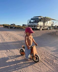 a young boy riding a wooden tricycle in the sand with an rv behind him