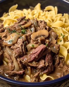 a blue bowl filled with pasta and meat covered in mushroom sauce on top of a wooden table