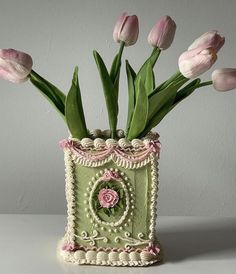 pink tulips are in a green vase on a white countertop, with an ornate border around the edges