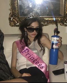 a woman sitting on top of a couch holding a blue bottle with pink ribbon around it