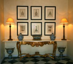 a table with four vases on it in front of some framed pictures and lamps