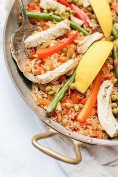 a pan filled with rice and vegetables on top of a white cloth next to a fork