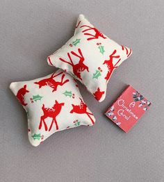 two red and green christmas pillows sitting on top of a gray surface next to a book