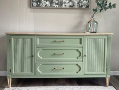 a green cabinet with three drawers and two vases on top of it in a room