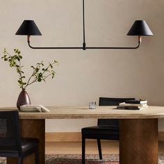 a dining table with two black lamps hanging from it's sides and a plant in the middle