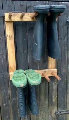 two green boots are hanging on the side of a wooden fence with pegs attached to it