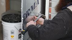 a man is working on the side of a building with a wrench and screwdriver