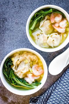 two bowls of soup with shrimp and spinach on the side next to spoons