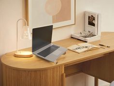 an open laptop computer sitting on top of a wooden desk next to a lamp and book