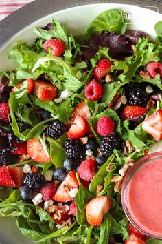 a salad with berries and nuts is on a plate next to a small bowl of dressing