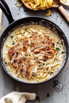 chicken alfredo in a skillet with parmesan cheese and bread on the side