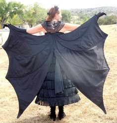 a woman in a black dress is holding up a large black bat shaped shawl