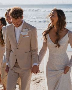 a man and woman are walking on the beach holding hands while wearing wedding attire with long sleeves