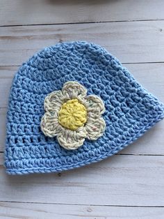 a crocheted blue hat with a flower on it sitting on a wooden surface