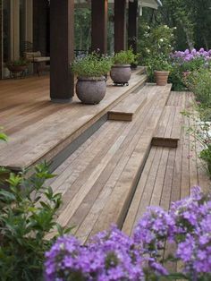 a wooden deck with potted plants and flowers on the bottom level next to it