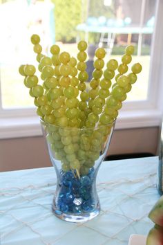 grapes are arranged in a glass vase on a table near a window with blue and green candies