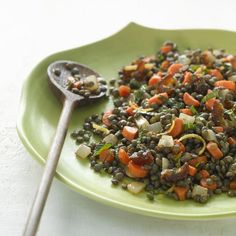 a green plate topped with lentils, carrots and other veggies next to a spoon