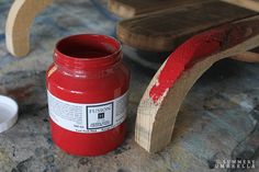 a red jar sitting on top of a table next to a wooden bench