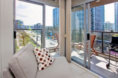 a living room filled with furniture and lots of windows next to a balcony overlooking the city