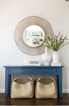 a blue table with two baskets underneath it and a mirror on the wall behind it