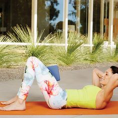 a woman is doing exercises on an orange yoga mat in front of a large building