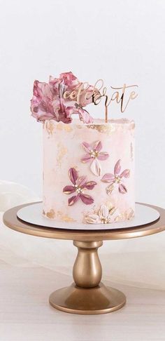 a cake with pink flowers on top is sitting on a gold plate and has the word love spelled in cursive writing