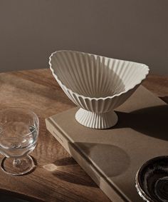 a white bowl sitting on top of a wooden table next to a glass and book