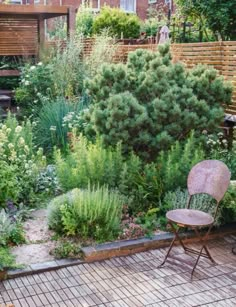 a chair sitting in the middle of a garden next to a wooden bench and shrubbery