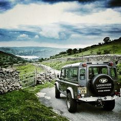 a jeep driving down a dirt road next to a stone wall and green grass covered hillside