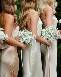 a group of women standing next to each other wearing dresses and holding bouquets with baby's breath