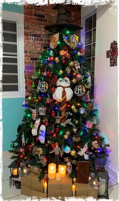 a decorated christmas tree with harry potter ornaments and candles in front of a brick wall