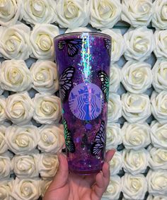 a hand holding a purple starbucks cup in front of white roses with the starbucks logo on it