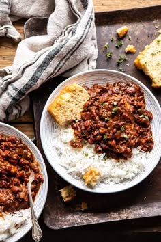 two plates with rice, beans and bread on a wooden table next to a towel