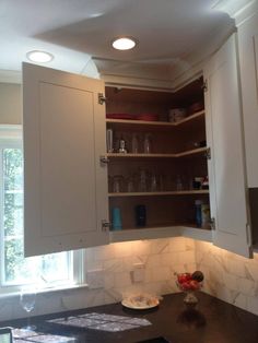 a kitchen with white cabinets and marble counter tops in front of a window that is lit by recessed lights